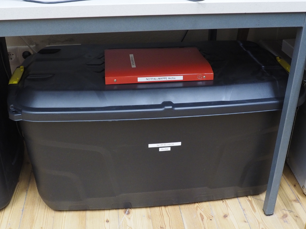 Geschlossene Notfallbox und Notfallmappe am Standort im Archivbüro: Unter einem Arbeitstisch ist die Box platzsparend aufbewahrt, ein Zugriff im Notfall trotzdem rasch möglich / (c) Schottenstift Wien (Foto: Rasinger) OLYMPUS DIGITAL CAMERA