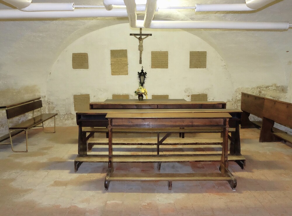 Gedenkraum Gruft / ÖOK/km Hier erkennt man den Gedenkraum der Mary Ward Gruft, Sitzbänke vor einem Kreuz, dahinter an den Wänden 8 Tafeln, die verstorbene zeigen, darunter auch Saint-Julien.