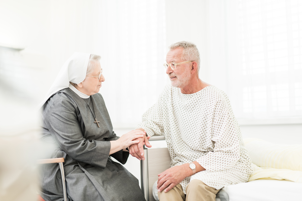 Eine Ordensfrau sitzt bei einem Patienten. 