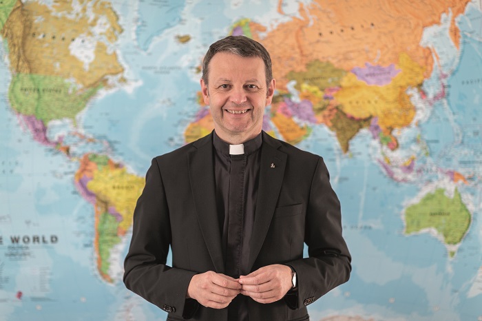 P. Christian Marte SJ mit einer Weltkarte im Hintergrund