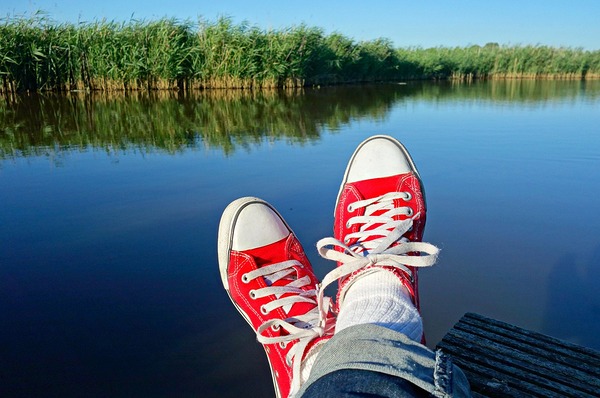 jemand liegt auf einem Steg bei einem See; er oder sie hat rote Turnschuhe an 