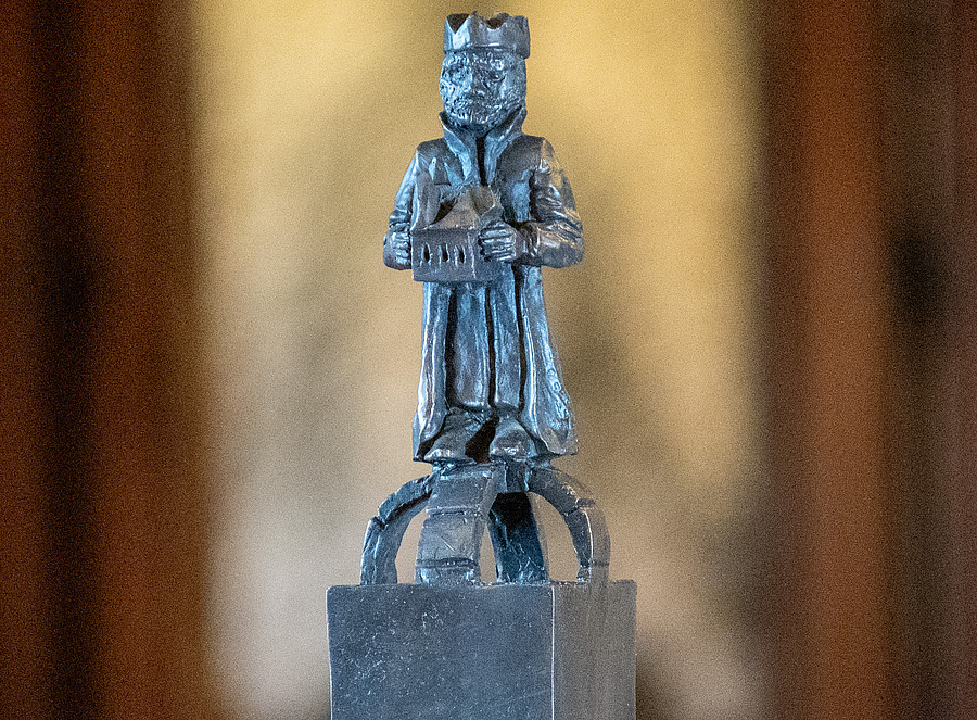 Der von Markus Redl neu gestaltete Hl. Leopold steht auf einem würfelartigen Sockel, der von einer Bogenstruktur bekrönt wird, die an die Kuppel eines Gebäudes oder den oberen Teil einer Krone erinnert.